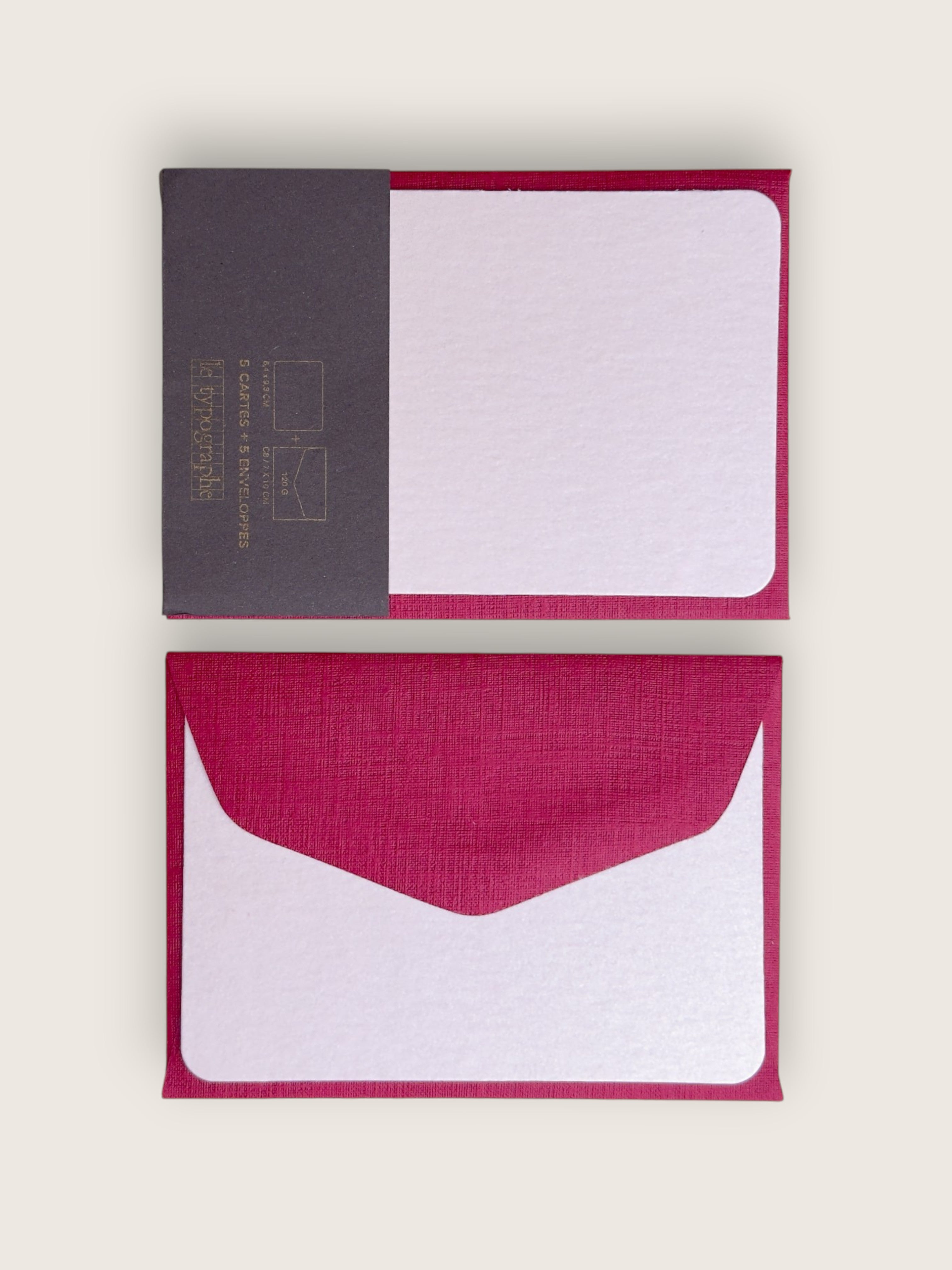 A set of minimalist stationery cards and envelopes on a light beige background. The set includes a closed card with a dark gray textured left panel and a magenta-pink right border, and an open matching envelope below it showing a white textured center with a magenta-pink border.
