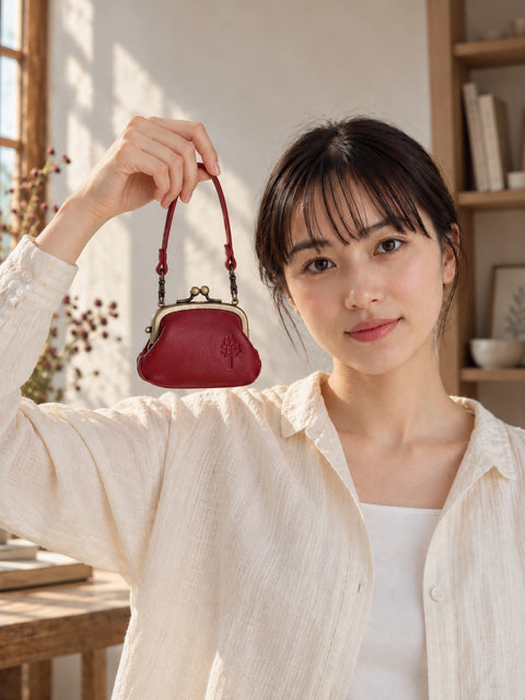 Woman holding up a deep red leather kiss lock coin purse by its handle