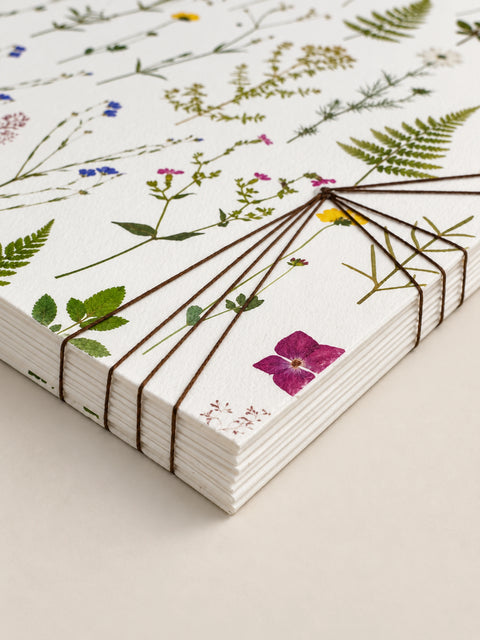 a handmade french notebook with delicate pressed floral and botanical illustrations, bound together with thin brown string on a light beige background.
