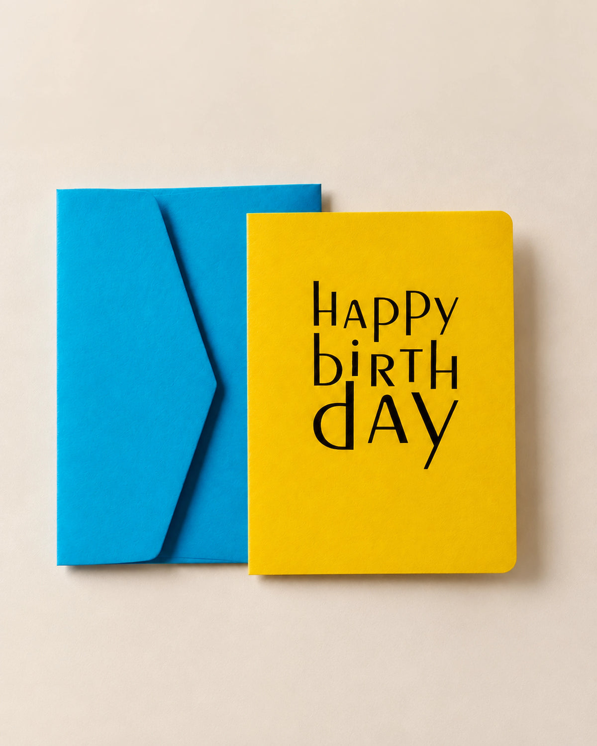 Yellow letterpress Happy Birthday card overlapping its cornflower blue envelope