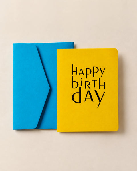 Yellow letterpress Happy Birthday card overlapping its cornflower blue envelope