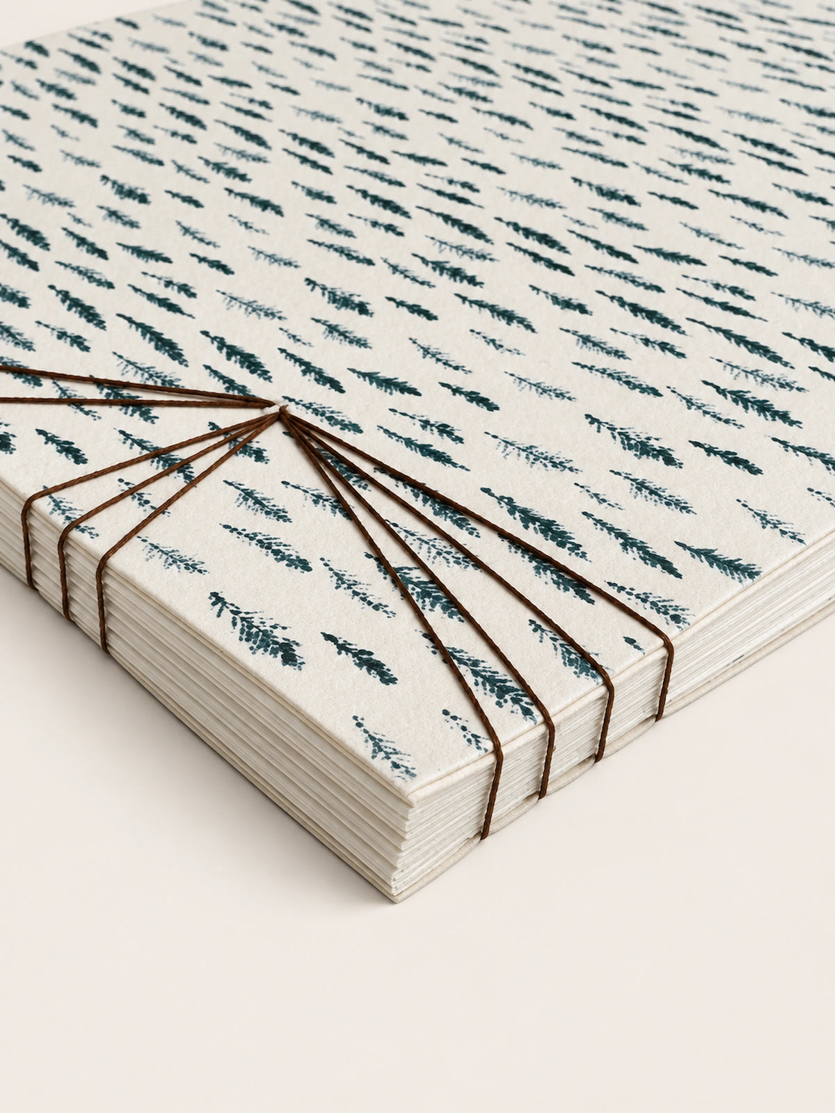 Close-up of a cream paper notebook with a blue hand-drawn pattern and exposed brown thread binding.