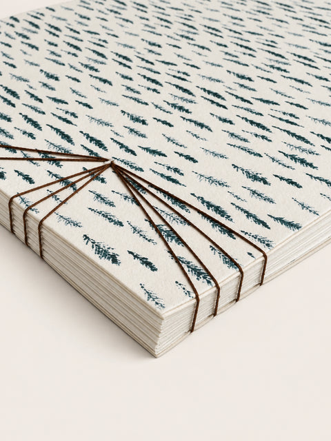 Close-up of a cream paper notebook with a blue hand-drawn pattern and exposed brown thread binding.