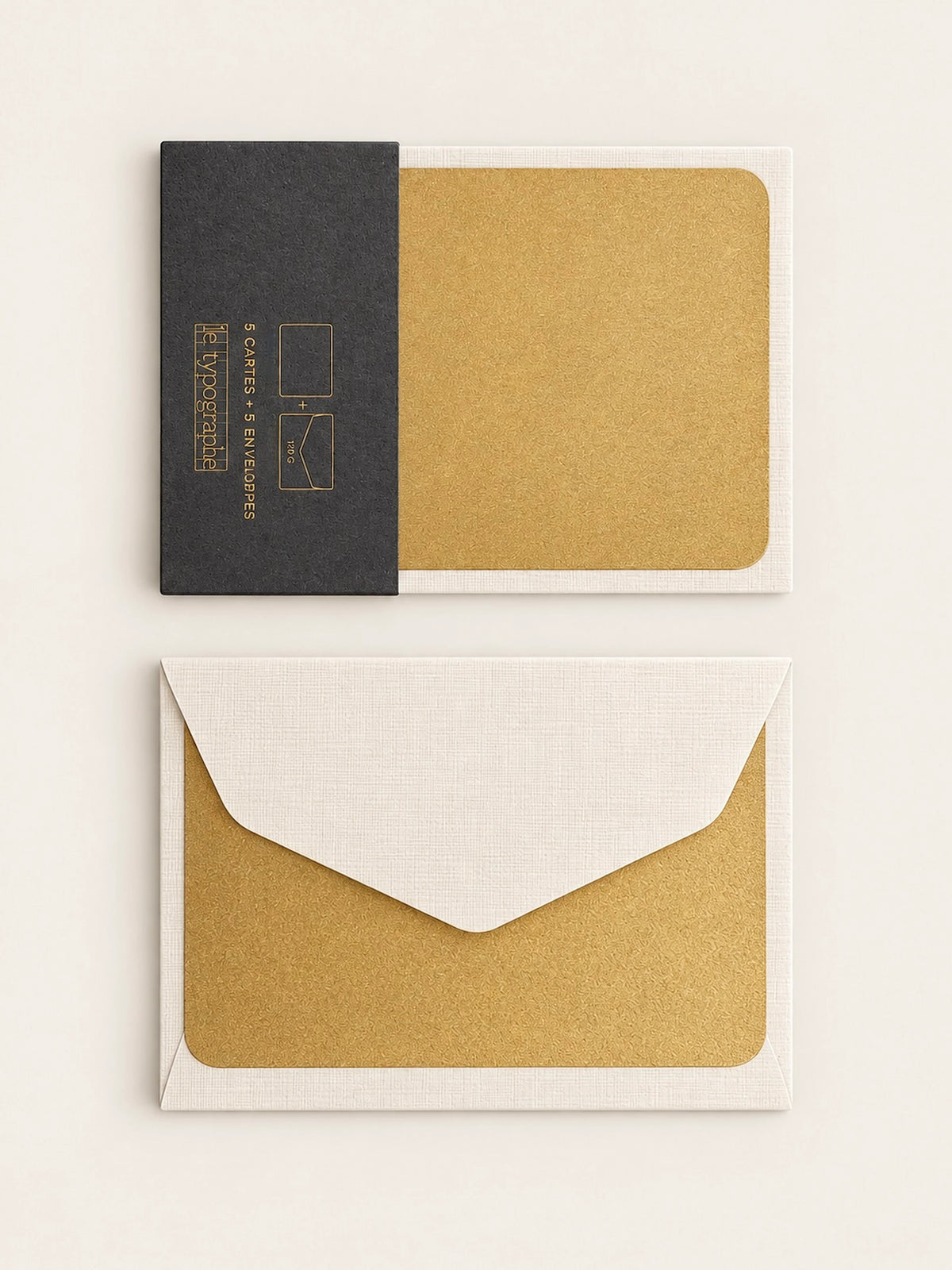 Gold letterpress note card held in its charcoal paper band, shown above a pale envelope with a second gold card behind the flap.