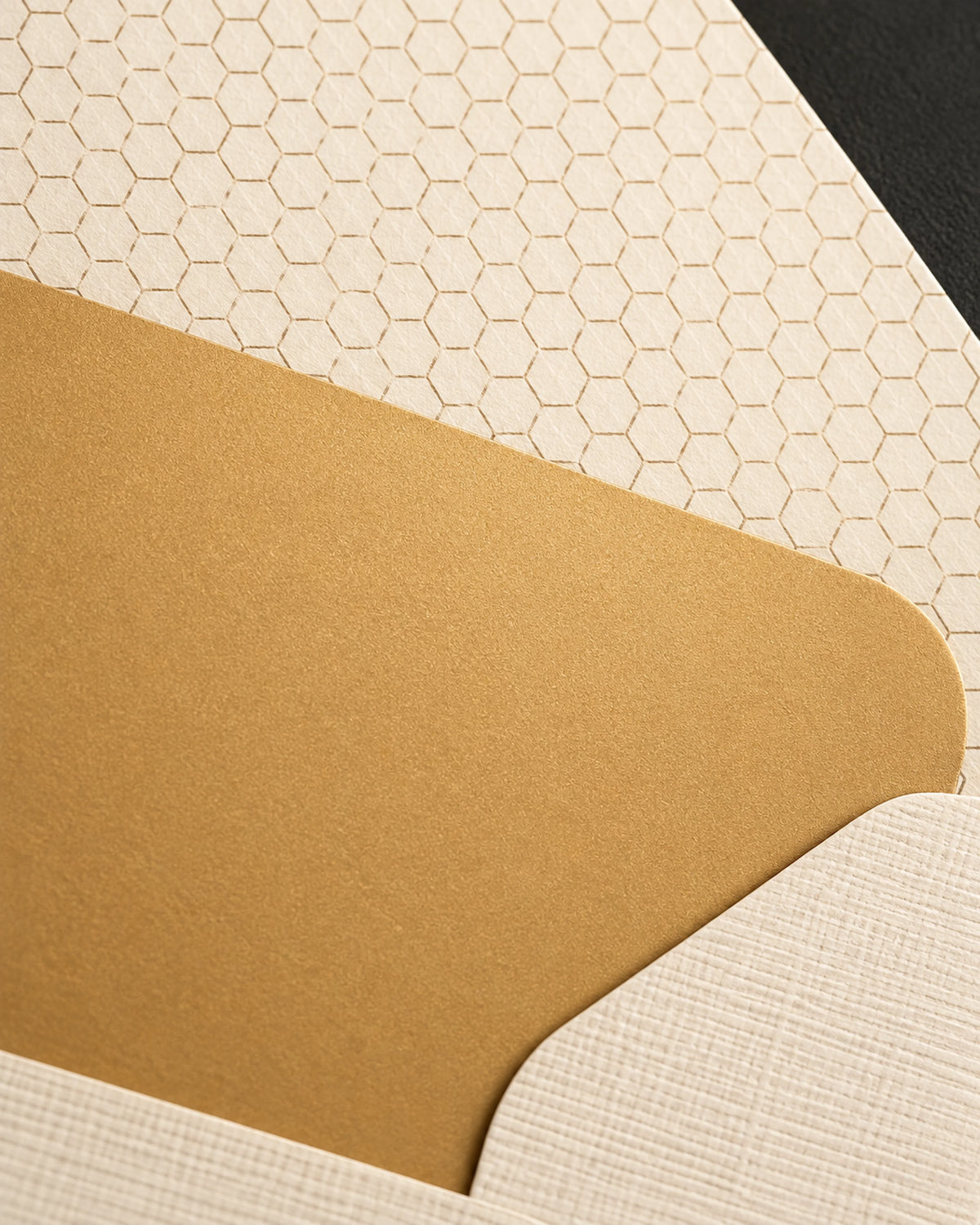 Close detail of a gold card against a pale envelope, showing the dark honeycomb pattern printed inside the envelope.