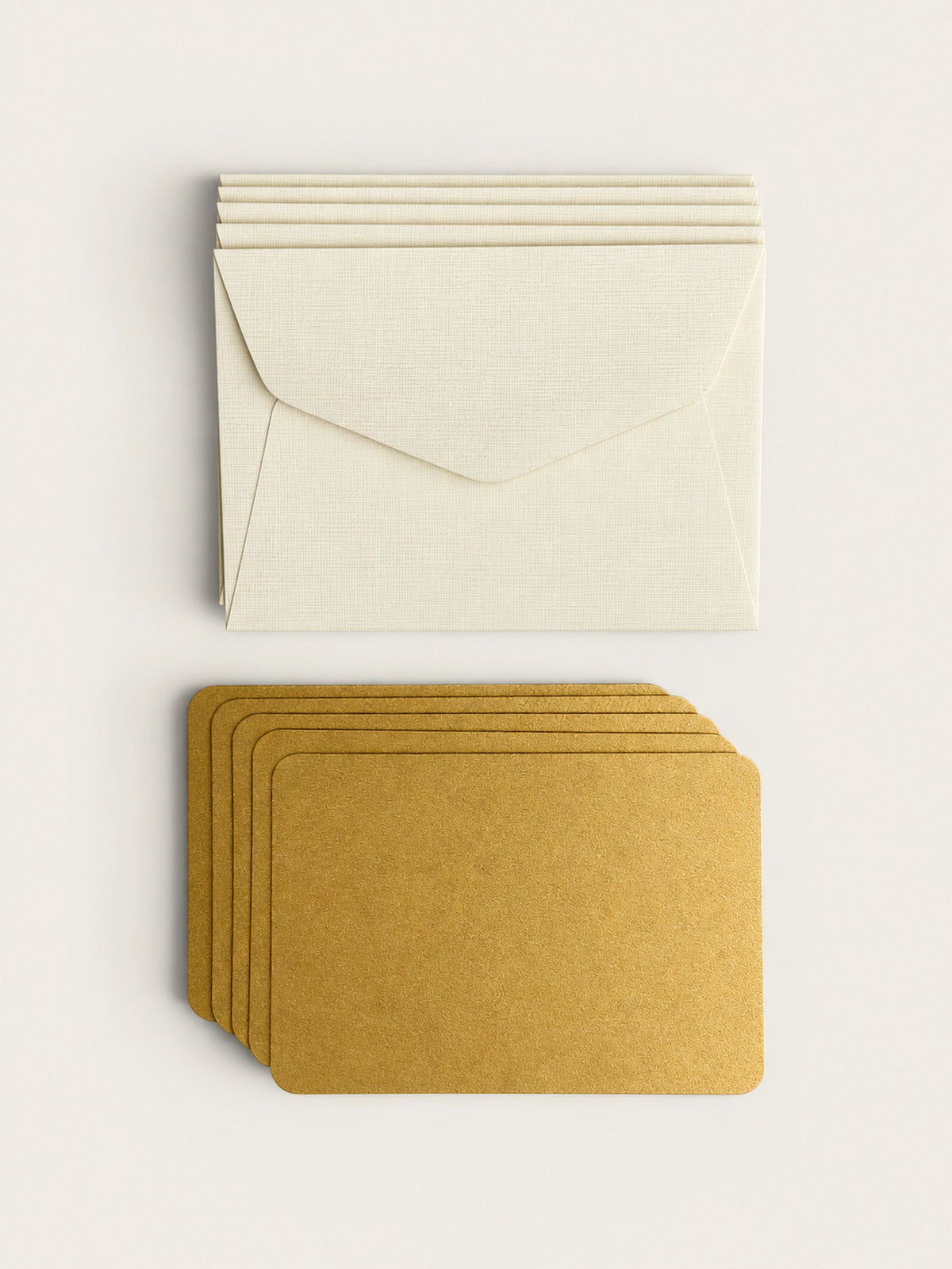 A stack of five pale envelopes above a stack of five gold letterpress note cards on a warm cream background.