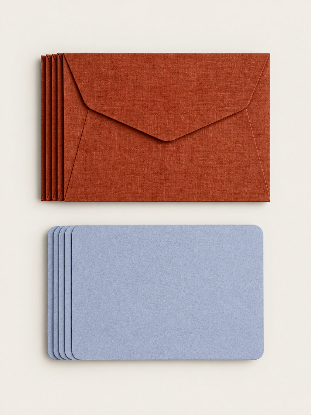 A stack of five cordyline envelopes above a stack of five lavender letterpress note cards on a warm cream background.