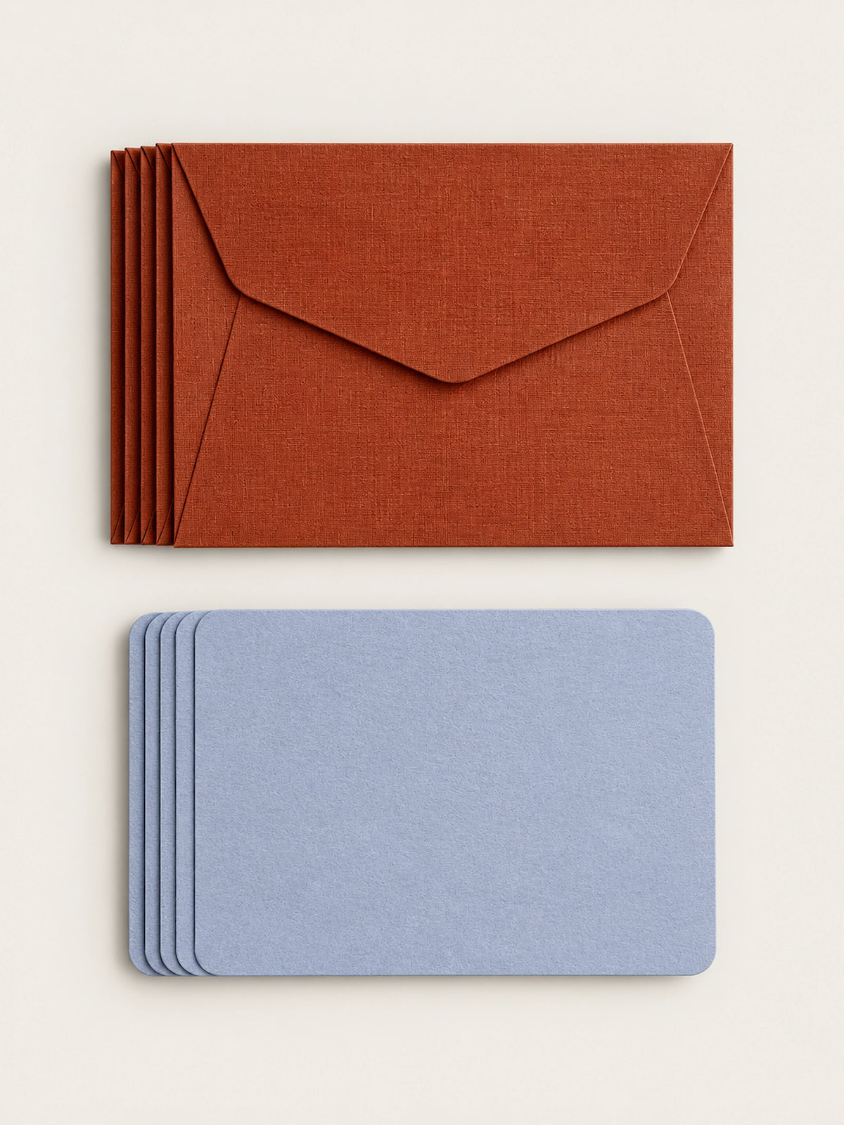 A stack of five cordyline envelopes above a stack of five lavender letterpress note cards on a warm cream background.