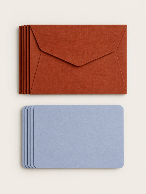 A stack of five cordyline envelopes above a stack of five lavender letterpress note cards on a warm cream background.