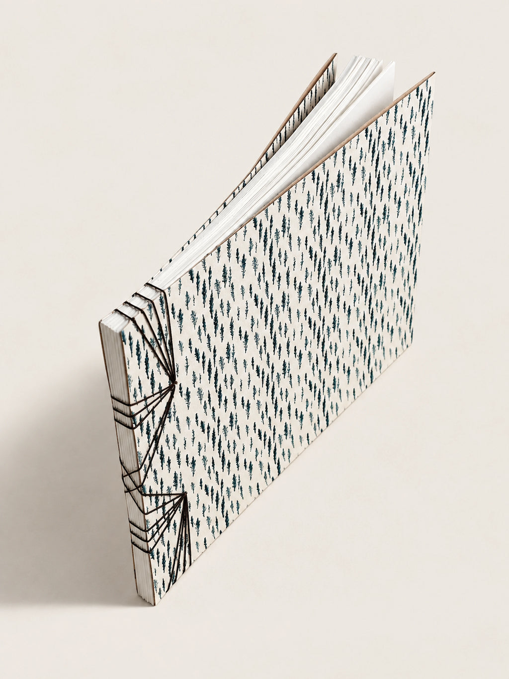 A handmade french notebook with a black and white geometric patterned cover, standing open at an angle on a light beige background.
