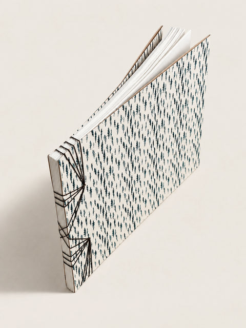 A handmade french notebook with a black and white geometric patterned cover, standing open at an angle on a light beige background.