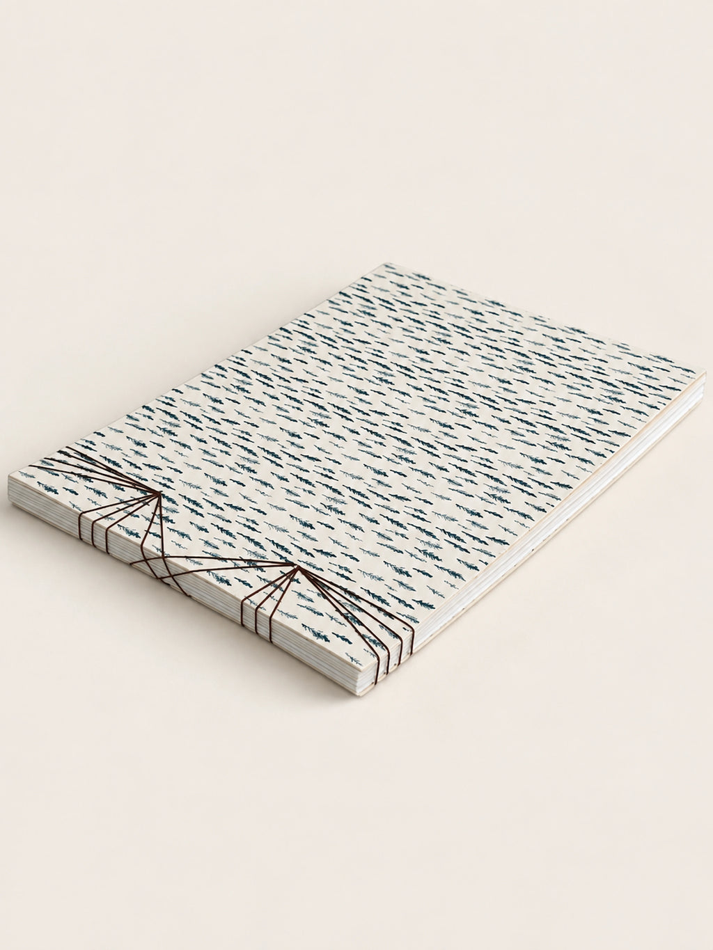 A french handmade notebook of patterned paper sheets bound with black string, photographed on a plain light beige background.