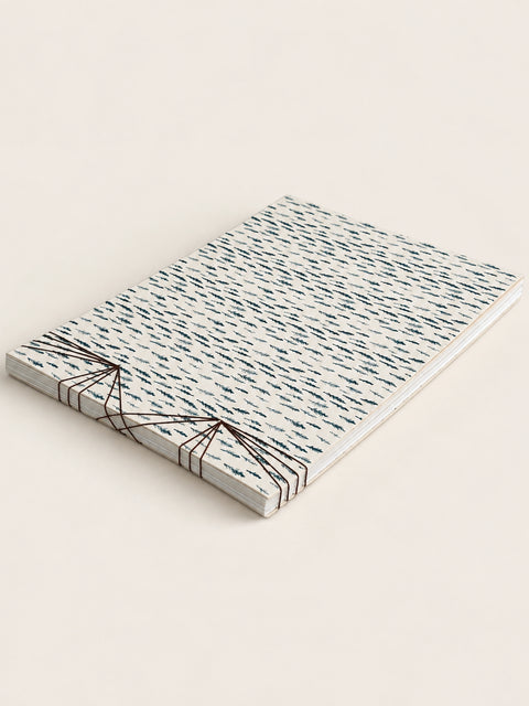 A french handmade notebook of patterned paper sheets bound with black string, photographed on a plain light beige background.