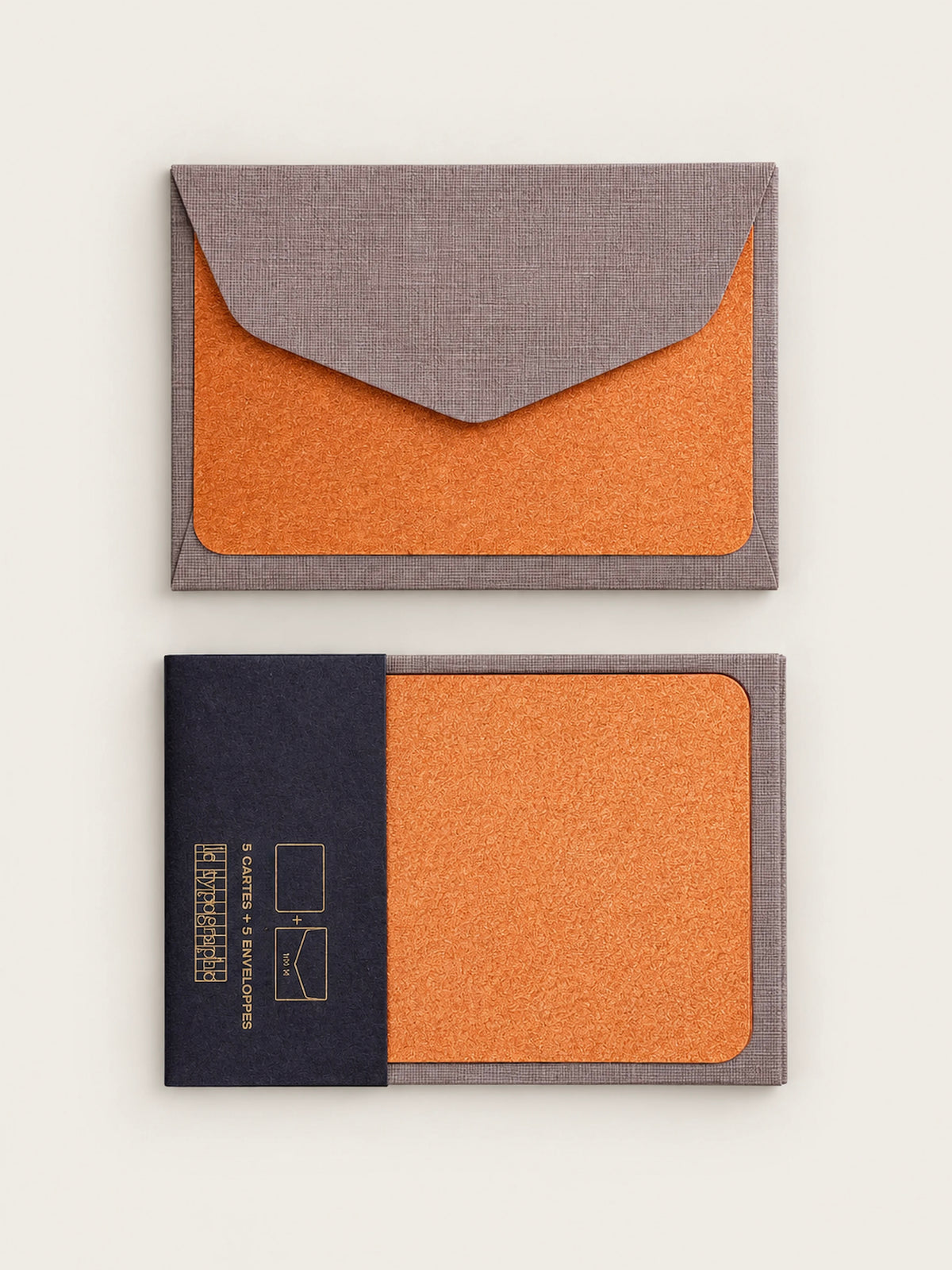 Copper letterpress note card tucked into a barley grey envelope, shown above a second card held in its charcoal paper band printed in gold.