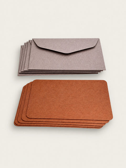 A stack of five barley grey envelopes above a stack of five copper letterpress note cards on a warm cream background.