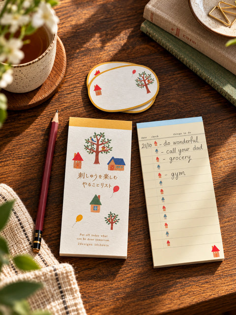 Japanese to-do list notepad with colourful houses, trees and balloons on a textured cover, displayed beside smooth lined checklist sheets and oval cards.