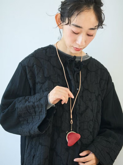 Woman in a black jacket wearing a deep red leather kiss lock purse on a long undyed leather cord