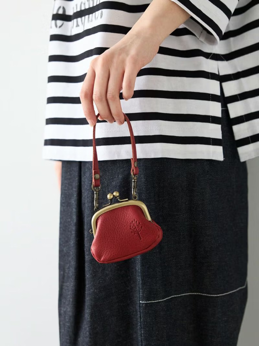 Deep red leather kiss lock coin purse carried by its short leather handle