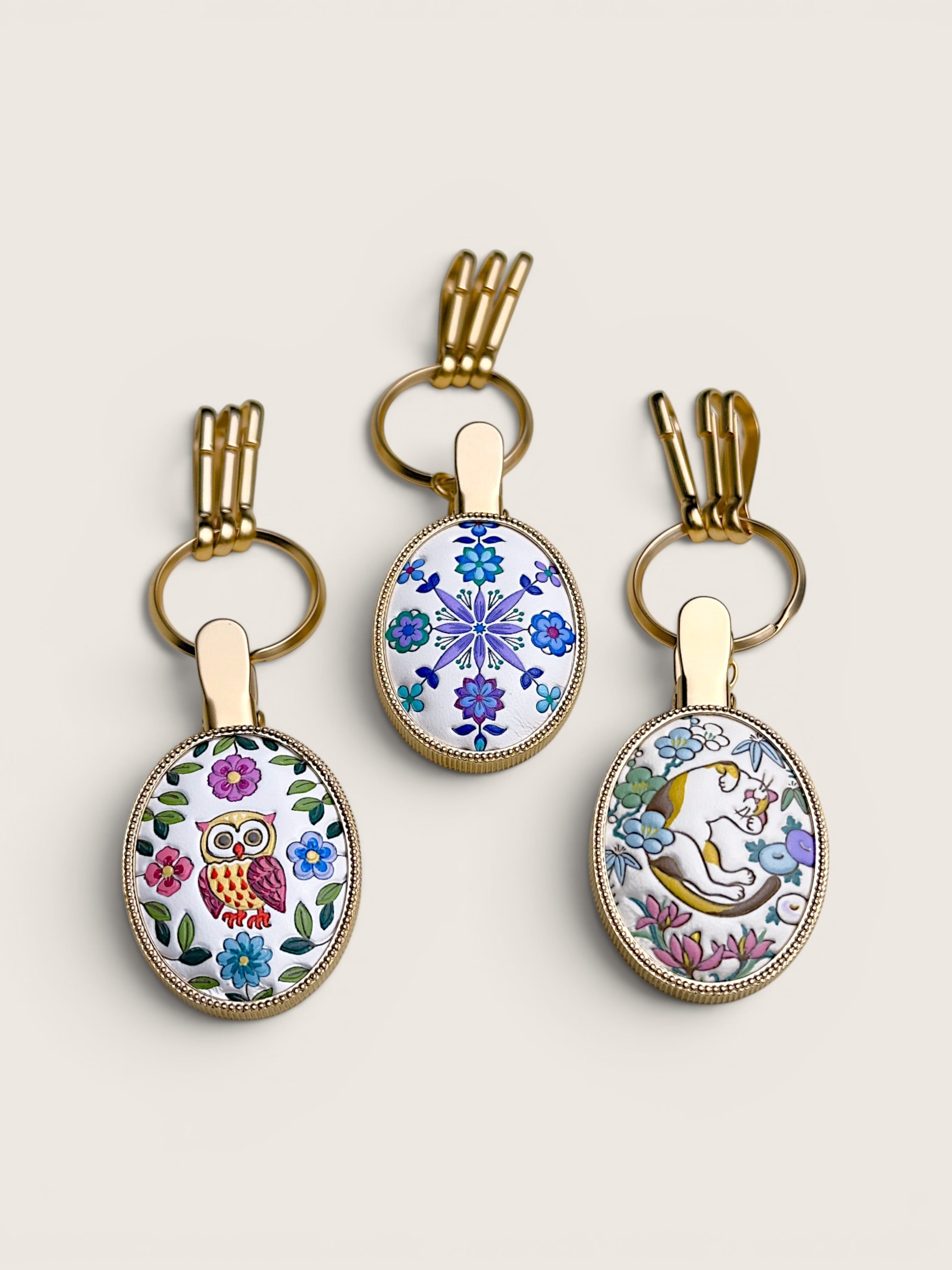 Ourooh Japanese Yuzen leather key clips with hand-painted owl, cat, and floral designs on brass frames.