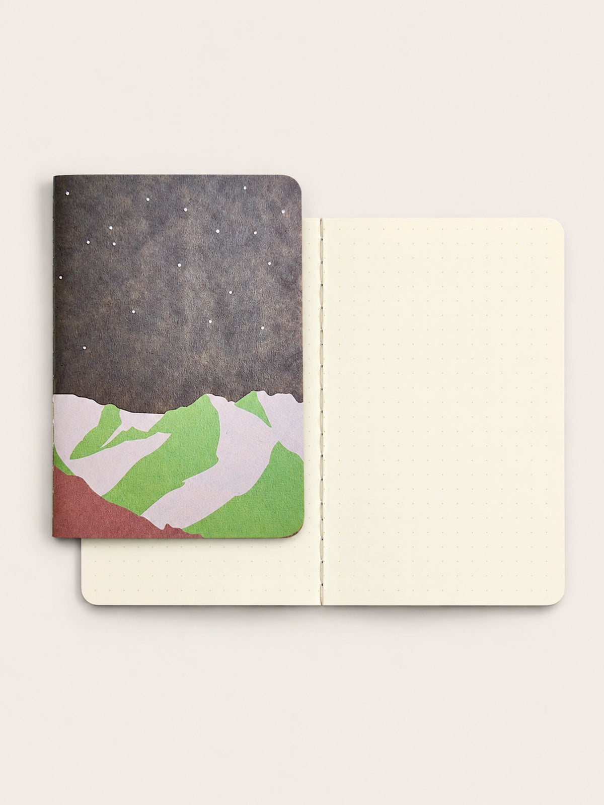RO-BIKI NOTE Mountain Night Japanese pocket notebook with starry charcoal cover and green mountain illustration, shown with open cream 5 mm dotted pages and thread stitching.