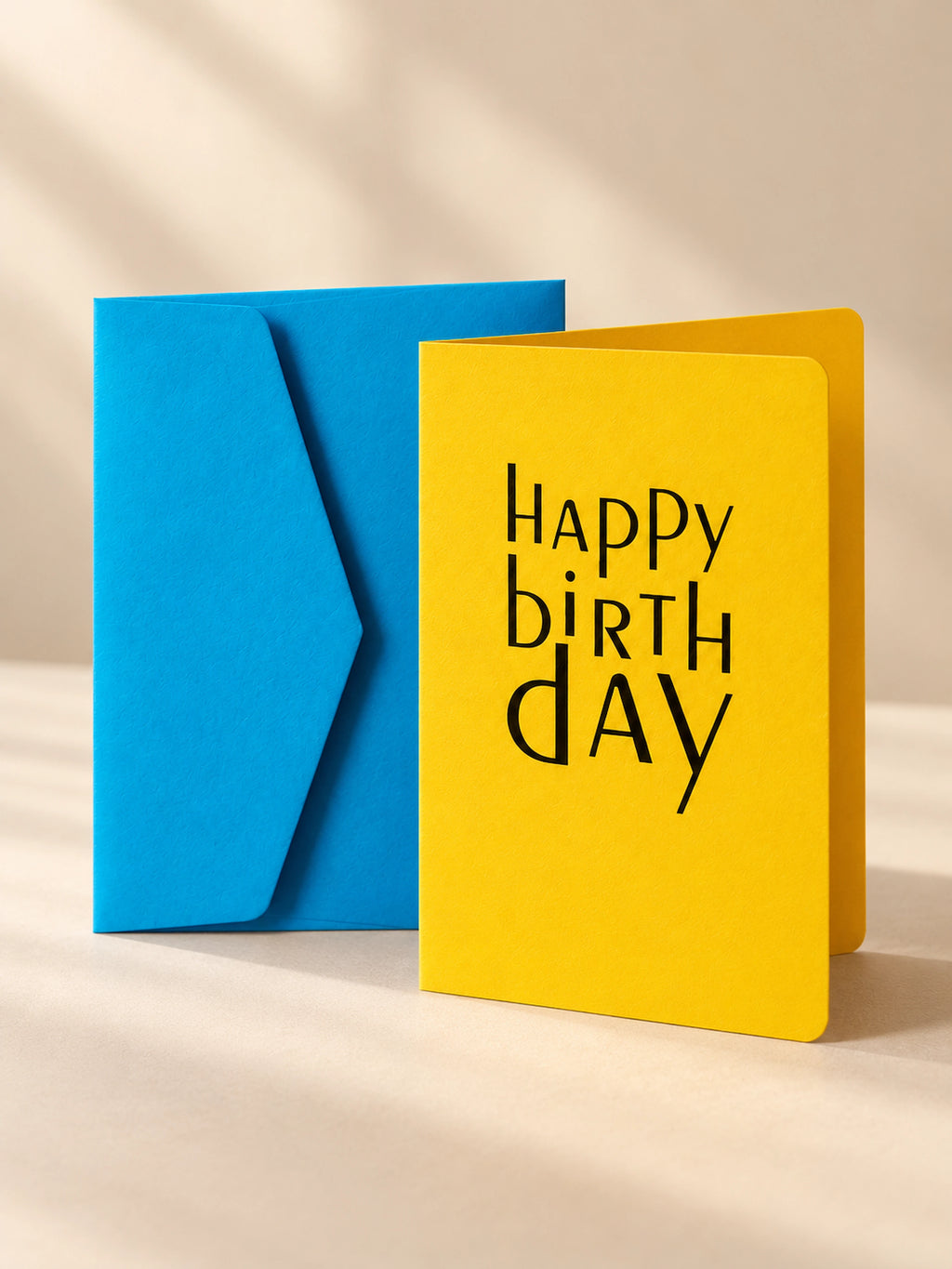 Banana yellow letterpress birthday card with dark blue lettering, standing open beside a cornflower blue envelope
