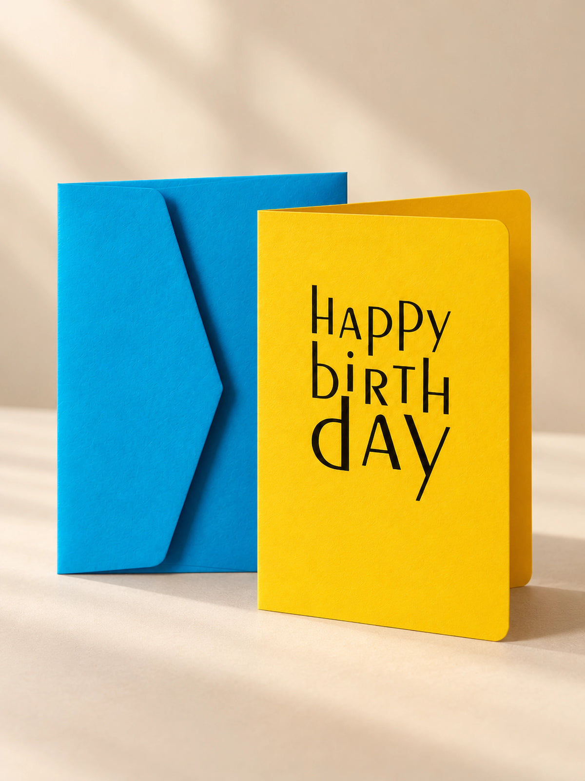Banana yellow letterpress birthday card with dark blue lettering, standing open beside a cornflower blue envelope